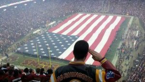 man saluting a large American flag at a football. game