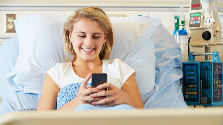 a young woman in her hospital bed smiling because she's taking advantage of health 2.0