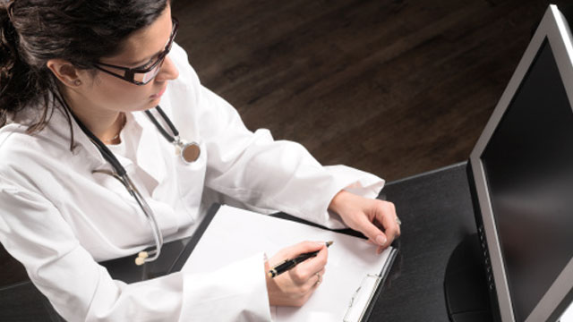 medical doctor writing and looking at computer screen