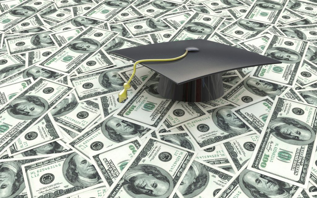 a graduation cap on a stack of 100 dollar bills