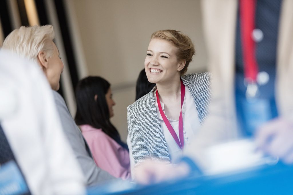 a young woman with a big smile looking at another woman at a conference