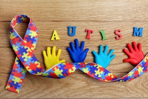 children's colorful alphabet letters spelling Autism with colorful hands and a ribbon with puzzle pattern on a horizontal wooden background