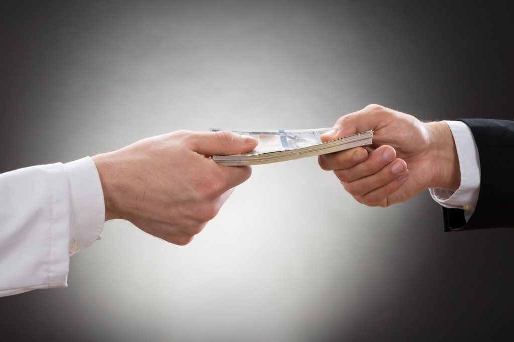 the hands of a doctor and business person with a stack of cash changing hands