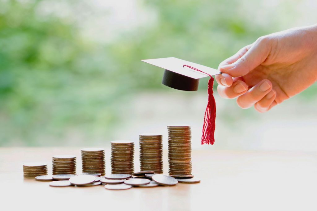 a tiny graduation cap and a sequence of coins stacked higher and higher the cap is being placed on the highest stack