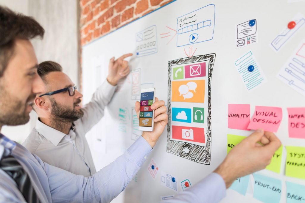 two guys working at a white board that are planning smartphone app developement