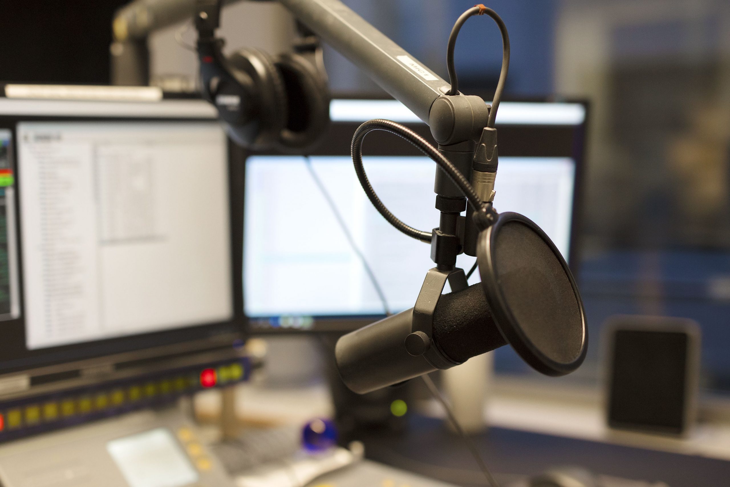 a studio microphone at a desk with computer monitors in the background