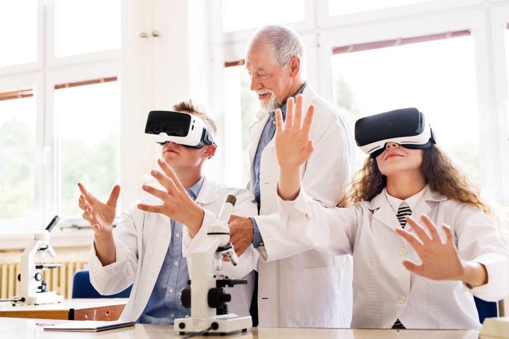 an older male doctor with two children in lab coats wearing virtual reality headsets and their arms are outstretched