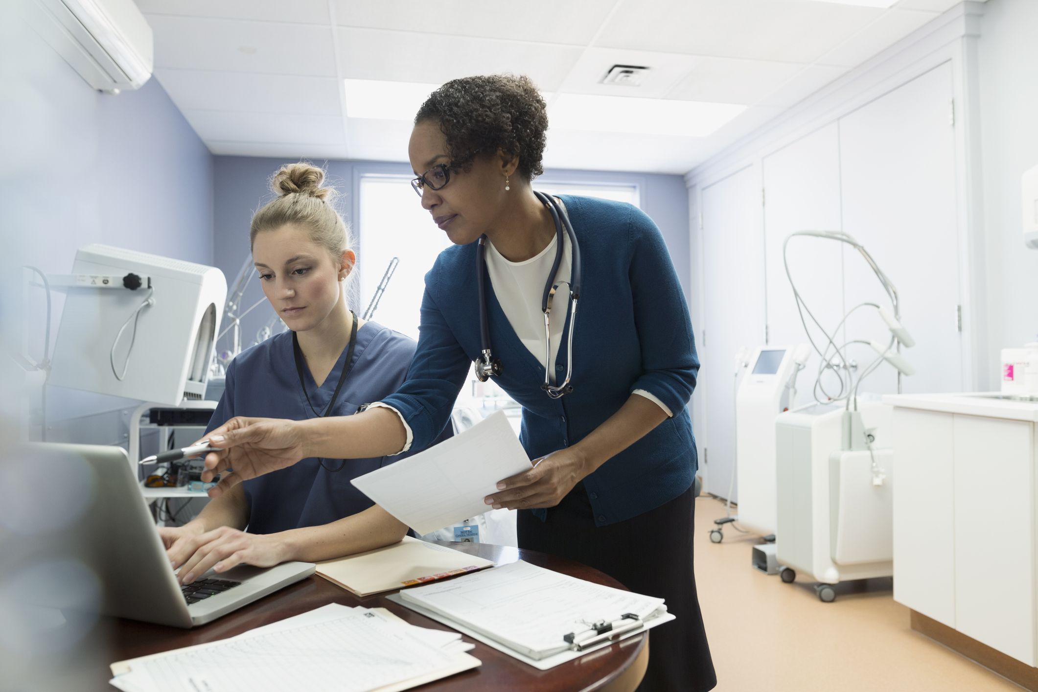 two medical professionals looking at a laptop in bright, cold examination room