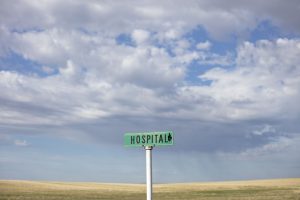 a street sign that says hospital with an arrow in a desolate field with open sky in the daytime