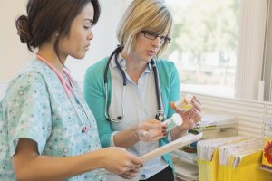 two female healthcare professionals looking at pill bottles in a healthcare facility with files in the background