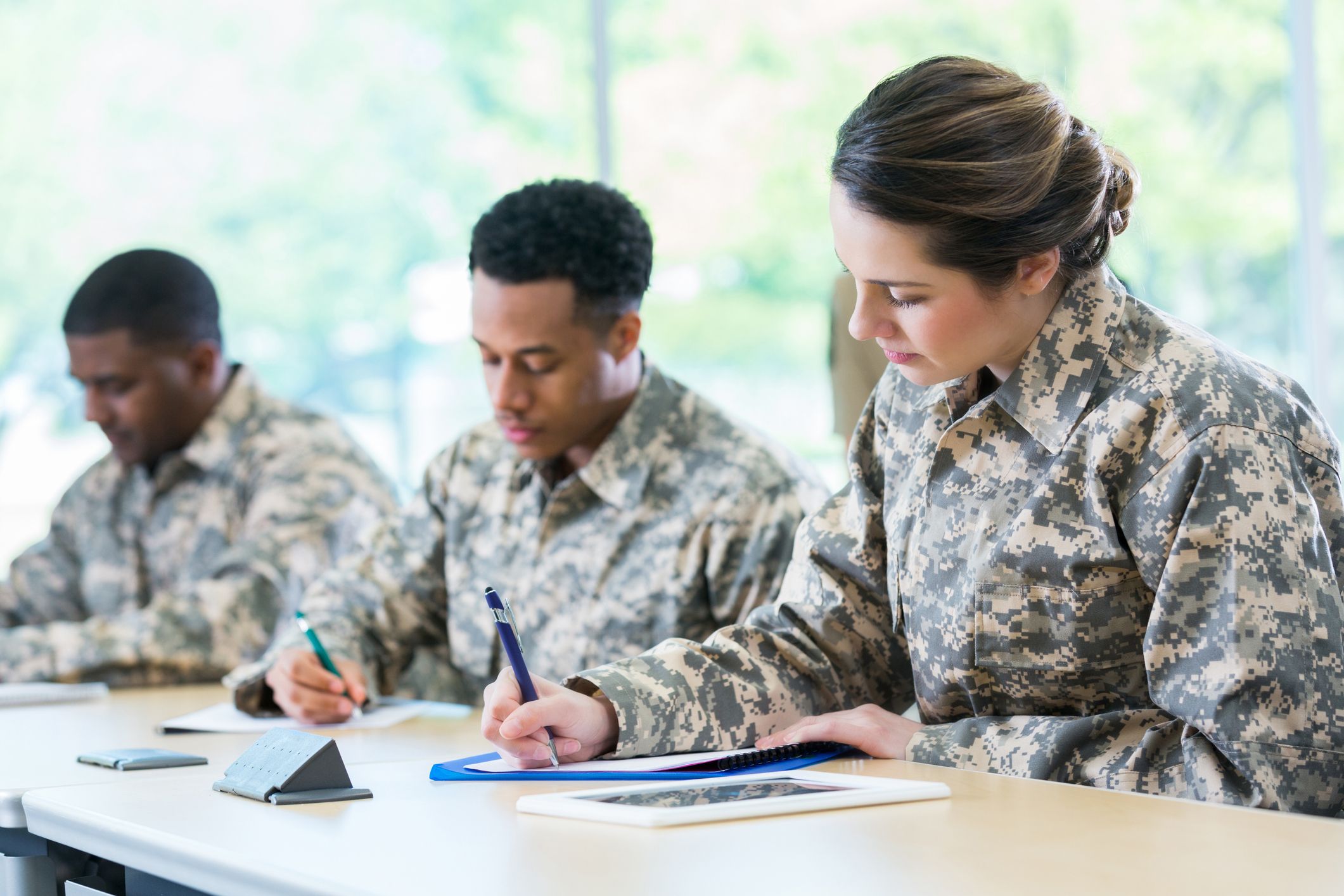 two men and a woman in army modern military fatigues taking a test in a room with big windows, daytime