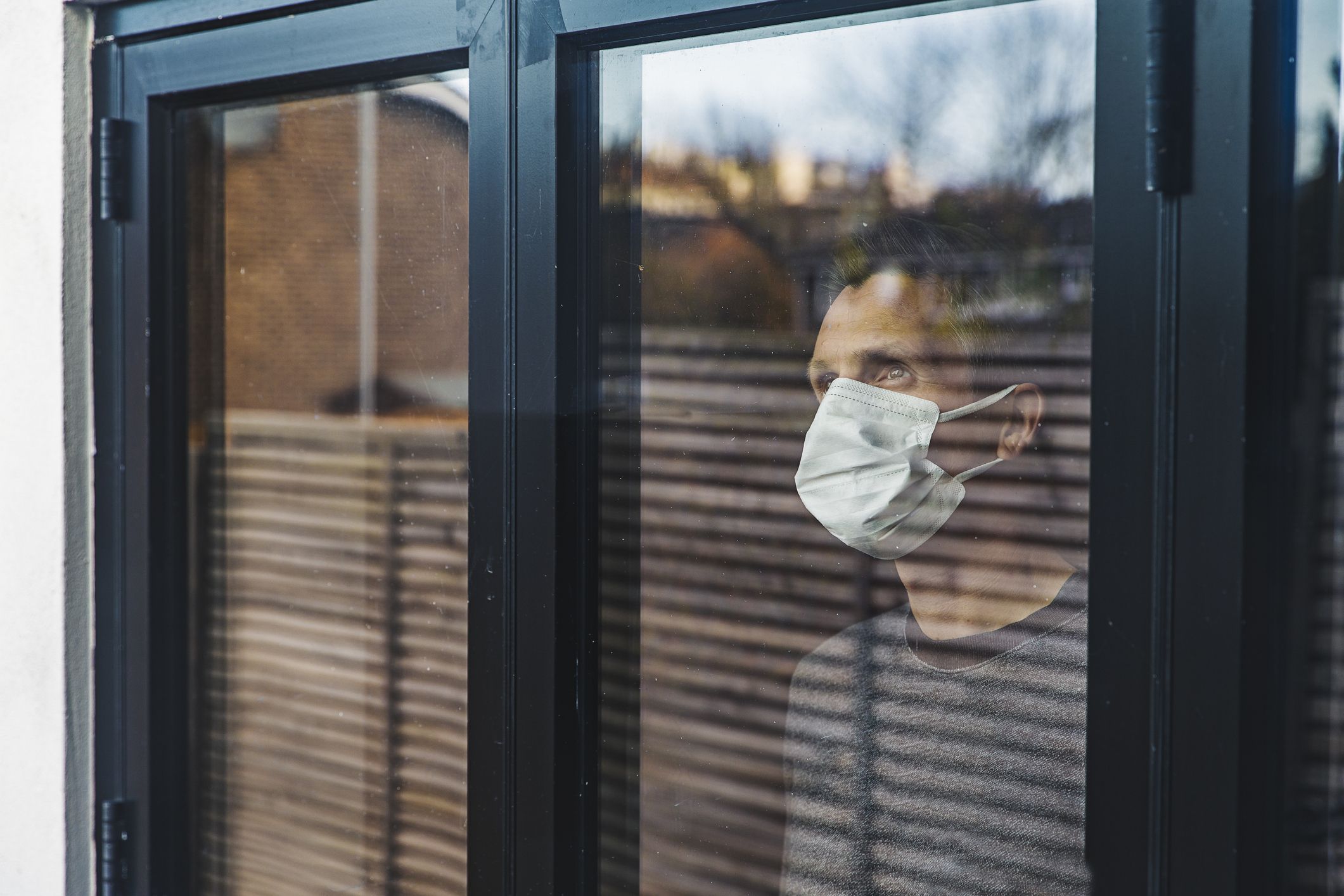 A man stands in his house wearing a mask.