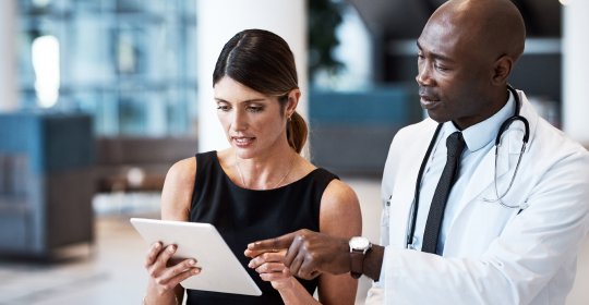 a male doctor and a female healthcare administrator looking at a tablet