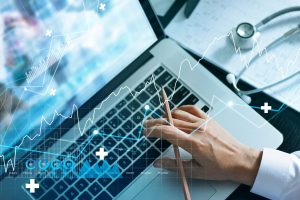 healthcare technology concept man's hand holding pencil resting on top of a laptop