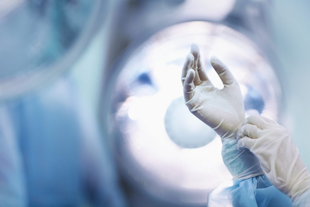 Surgeon adjusting glove in operating room.