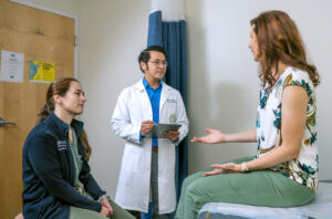 A doctor discusses a patient's concerns during an appointment while another healthcare professional listens.