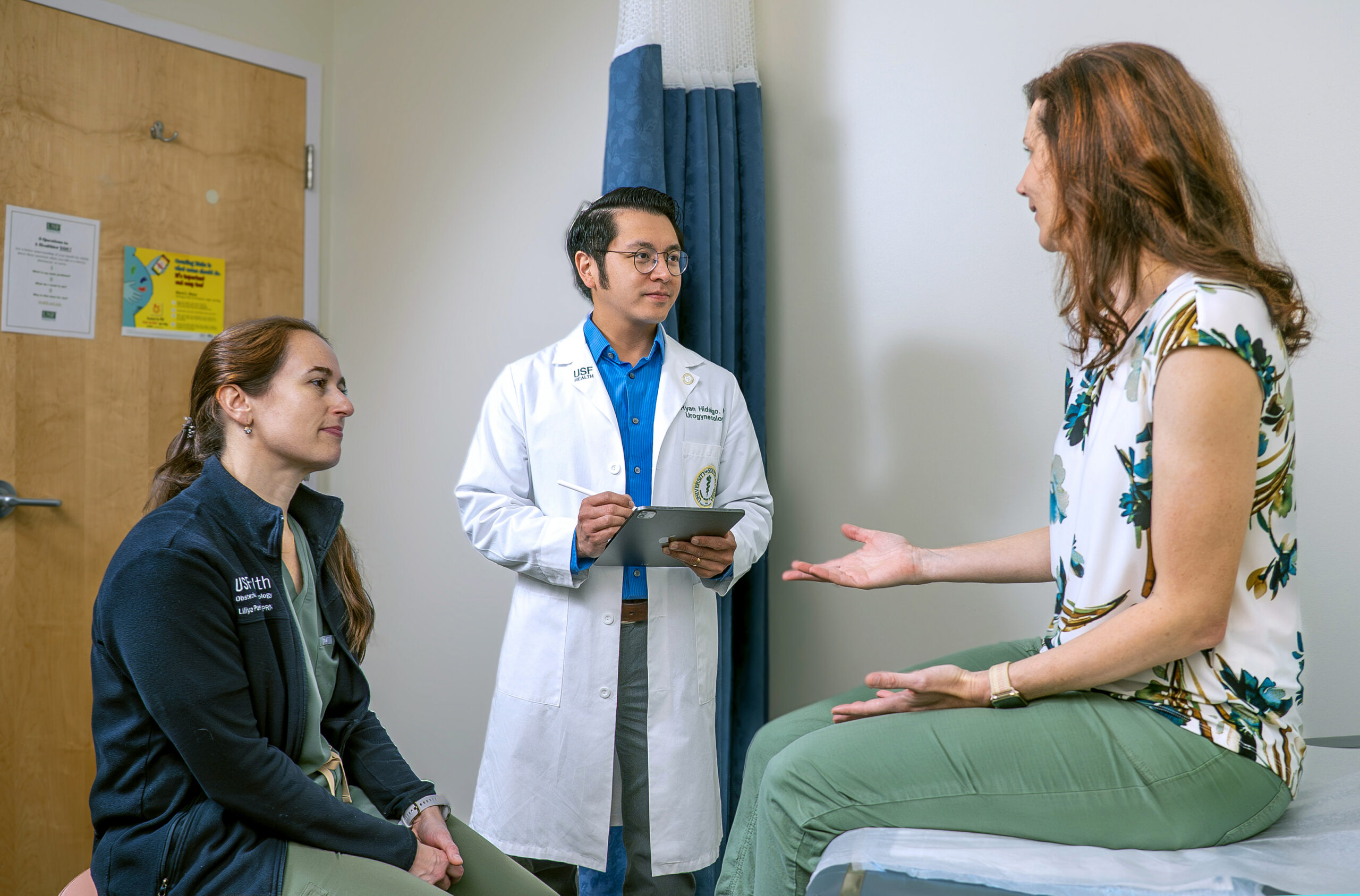 A doctor discusses a patient's concerns during an appointment while another healthcare professional listens.